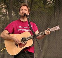 photo of David Rovics singing and playing guitar in concert