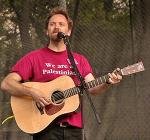 photo of David Rovics singing and playing guitar in concert