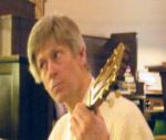 photo of Tom Allen playing guitar in front of what appears to be a pile of wooden crates.