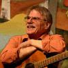 photo of Gordon Bok smiling and seated with his guitar on his lap